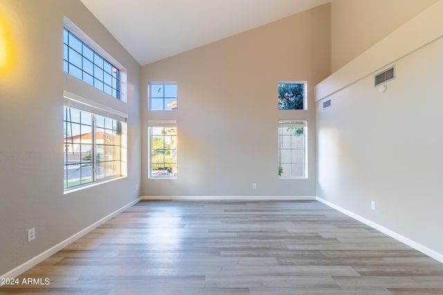 empty room featuring a healthy amount of sunlight, light hardwood / wood-style floors, and high vaulted ceiling