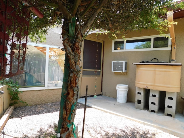 view of exterior entry with a wall unit AC and stucco siding