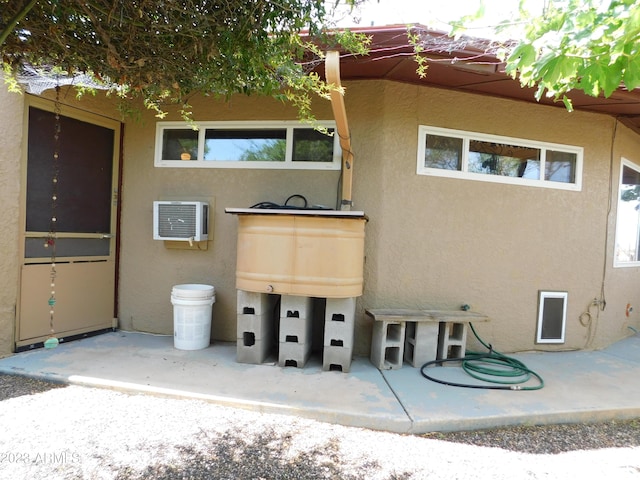 rear view of house with stucco siding, an AC wall unit, and a patio