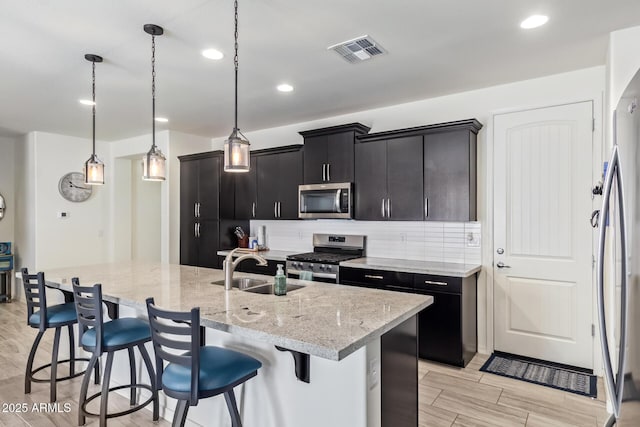 kitchen with visible vents, appliances with stainless steel finishes, a center island with sink, and pendant lighting