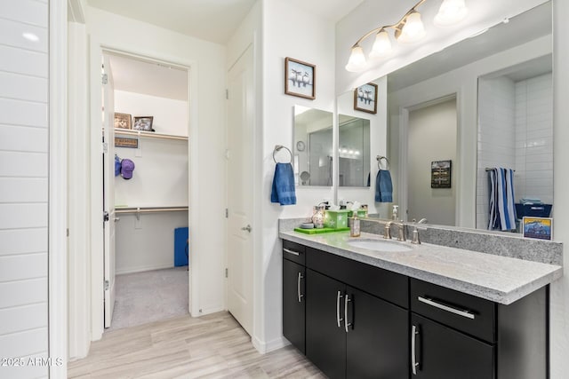 full bath featuring baseboards, a walk in closet, wood finished floors, and vanity