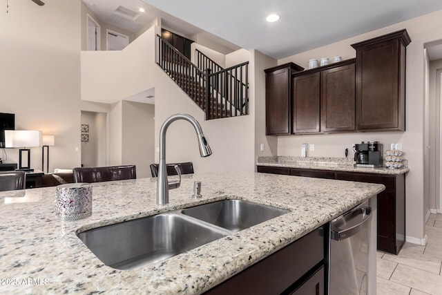 kitchen featuring dark brown cabinets, light stone countertops, dishwasher, light tile patterned floors, and a sink