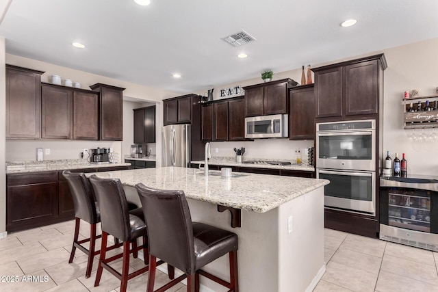 kitchen featuring visible vents, a center island with sink, a sink, stainless steel appliances, and light tile patterned floors