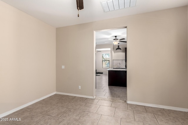 empty room featuring light tile patterned flooring, baseboards, visible vents, and ceiling fan