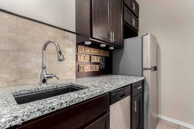 kitchen with a sink, light stone counters, backsplash, stainless steel appliances, and dark brown cabinetry