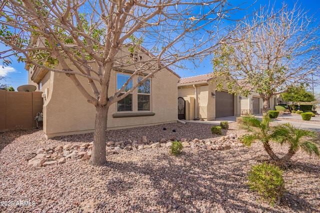 view of front of home featuring stucco siding, driveway, fence, a garage, and a tiled roof