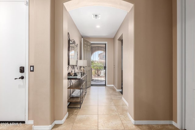 doorway with light tile patterned floors, baseboards, visible vents, and arched walkways