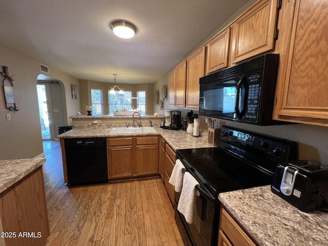 19943 N 77th Ave, Glendale, AZ 85308 - kitchen with black appliances, a peninsula, light wood finished floors, arched walkways, and decorative light fixtures