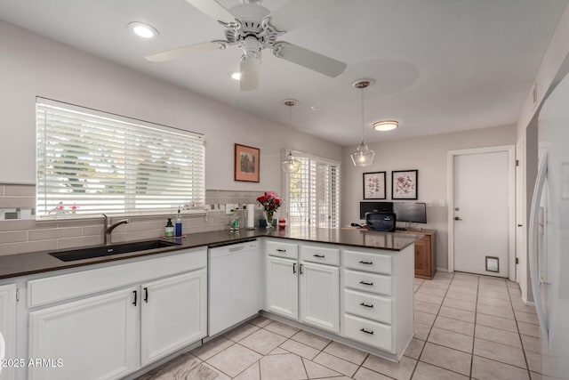 kitchen with a peninsula, white appliances, white cabinets, dark countertops, and a sink