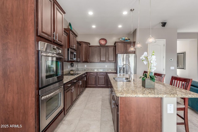 kitchen featuring a sink, appliances with stainless steel finishes, a breakfast bar, a kitchen island with sink, and pendant lighting