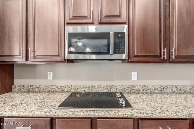 kitchen featuring stainless steel microwave, black electric stovetop, dark brown cabinets, and light stone countertops