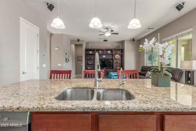 kitchen featuring a sink, open floor plan, a ceiling fan, decorative light fixtures, and light stone countertops