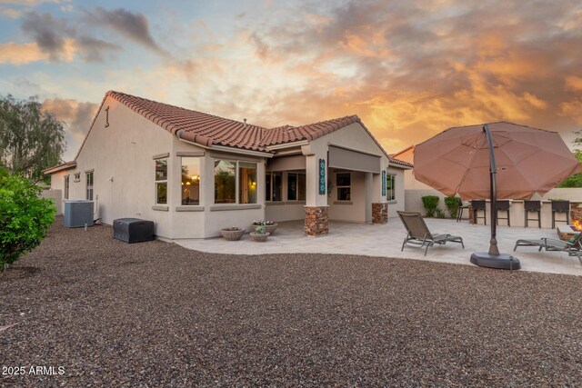back of property at dusk with a tile roof, a patio area, central AC, and stucco siding