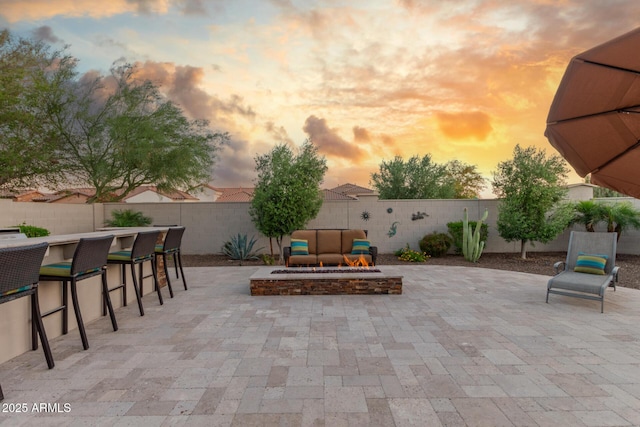 patio terrace at dusk with an outdoor fire pit and a fenced backyard