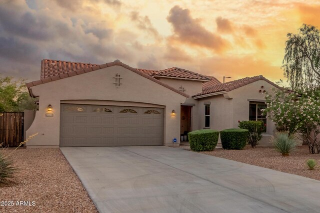 mediterranean / spanish home with an attached garage, driveway, a tiled roof, and stucco siding