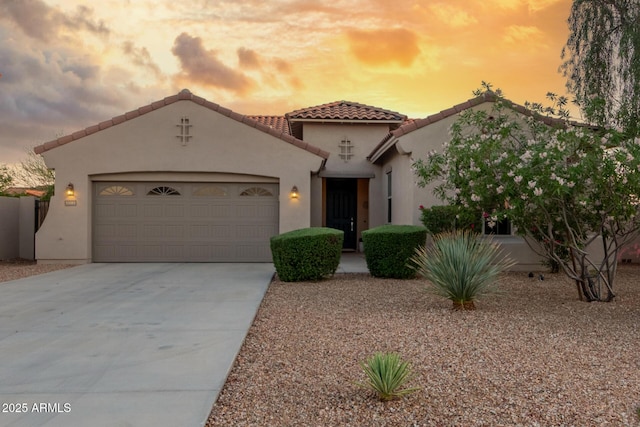 mediterranean / spanish house with an attached garage, a tile roof, concrete driveway, and stucco siding
