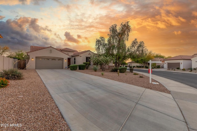mediterranean / spanish-style home featuring stucco siding, a tile roof, concrete driveway, an attached garage, and fence