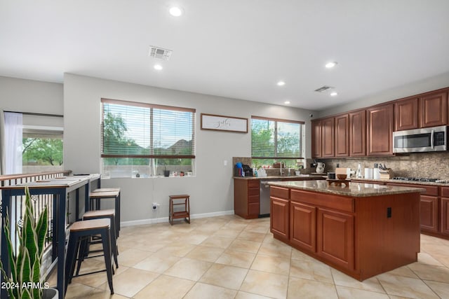 kitchen with light tile patterned flooring, a kitchen island, tasteful backsplash, dark stone countertops, and stainless steel appliances