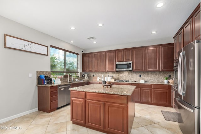 kitchen featuring a kitchen island, tasteful backsplash, light tile patterned floors, stainless steel appliances, and light stone countertops