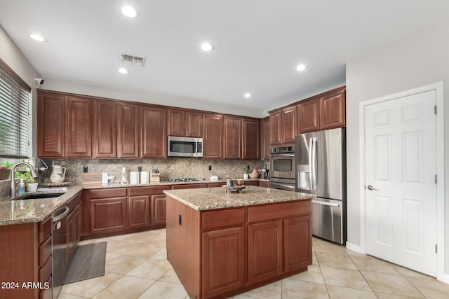 kitchen with sink, appliances with stainless steel finishes, backsplash, a center island, and light stone counters