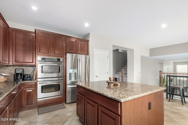 kitchen featuring stainless steel appliances, light stone countertops, a center island, and backsplash