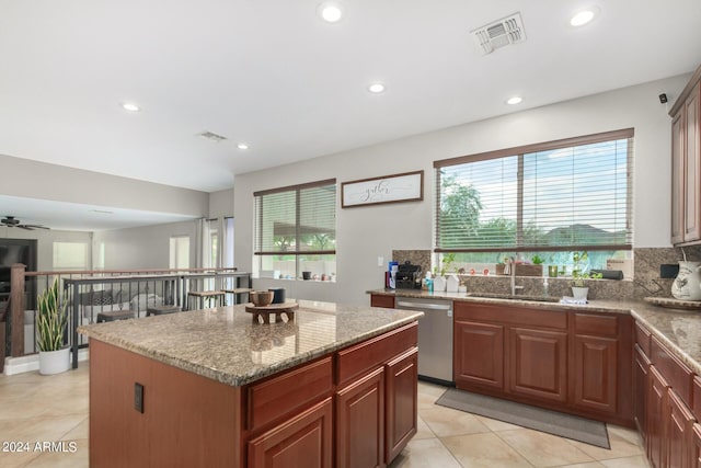 kitchen with light stone counters, stainless steel dishwasher, sink, and a kitchen island