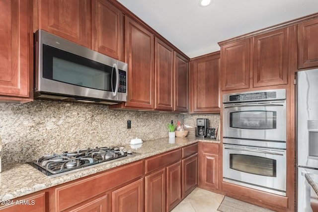 kitchen with appliances with stainless steel finishes, light tile patterned floors, light stone counters, and decorative backsplash