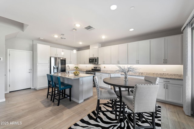 kitchen featuring a kitchen island, decorative light fixtures, a kitchen bar, stainless steel appliances, and light stone countertops