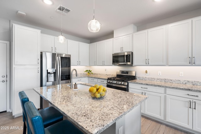 kitchen with sink, stainless steel appliances, decorative light fixtures, and a kitchen island with sink