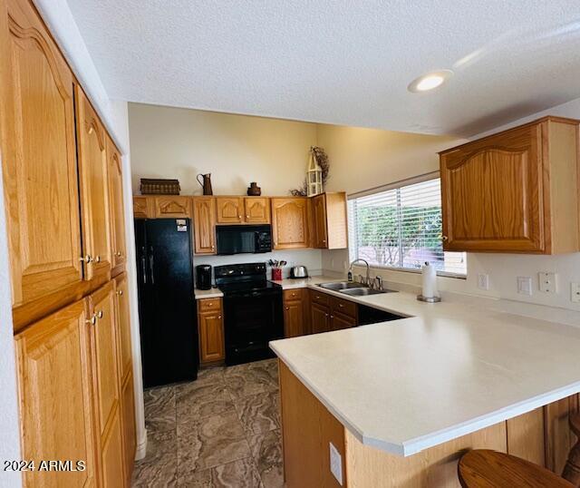 kitchen with sink, kitchen peninsula, a textured ceiling, a breakfast bar area, and black appliances