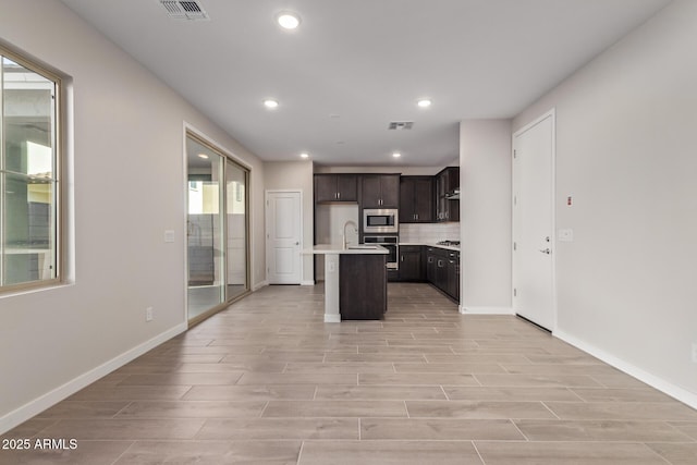 kitchen featuring appliances with stainless steel finishes, decorative backsplash, sink, light hardwood / wood-style flooring, and an island with sink