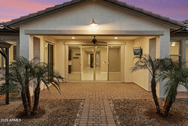 back house at dusk featuring ceiling fan and a patio