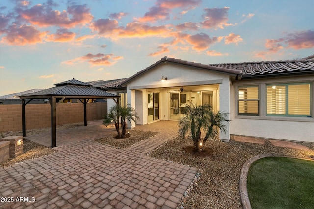 back house at dusk with a gazebo, ceiling fan, and a patio area