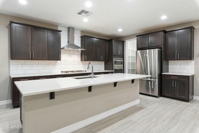 kitchen with wall chimney exhaust hood, stainless steel appliances, a breakfast bar, sink, and a kitchen island with sink