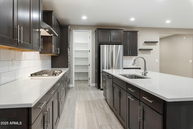 kitchen with appliances with stainless steel finishes, sink, wall chimney exhaust hood, an island with sink, and dark brown cabinets