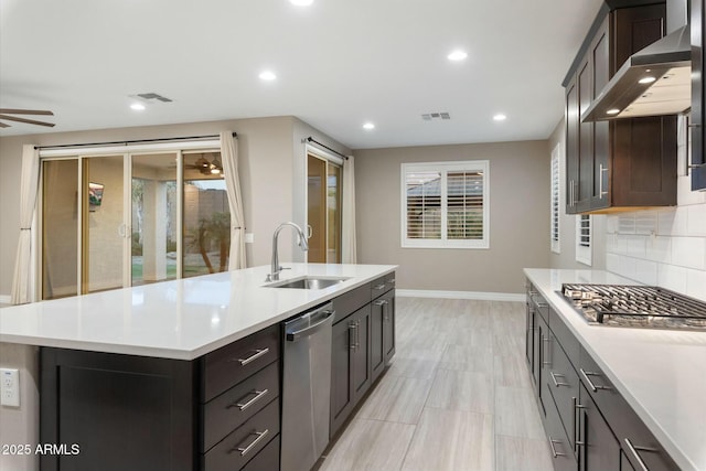 kitchen featuring a center island with sink, stainless steel appliances, sink, backsplash, and wall chimney exhaust hood