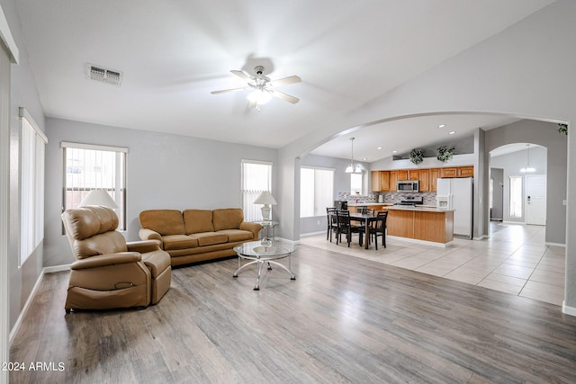 living room with ceiling fan with notable chandelier, light wood-type flooring, and vaulted ceiling