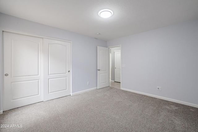 unfurnished bedroom featuring a textured ceiling, light colored carpet, and a closet