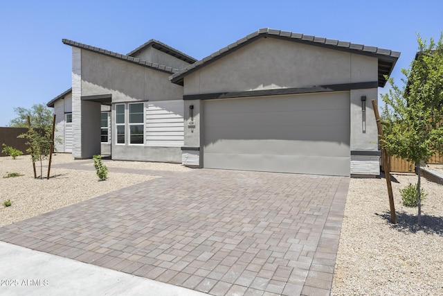 modern home with decorative driveway, fence, an attached garage, and stucco siding