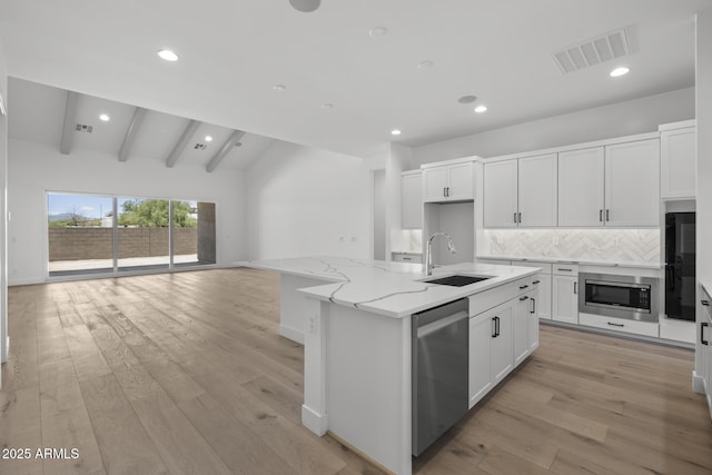 kitchen featuring a sink, visible vents, white cabinetry, appliances with stainless steel finishes, and a center island with sink