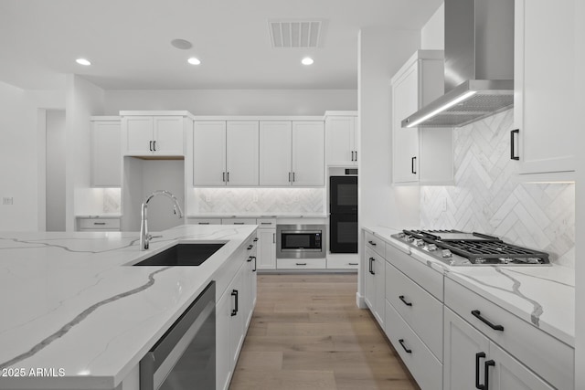 kitchen with visible vents, white cabinets, wall chimney exhaust hood, light stone countertops, and a sink