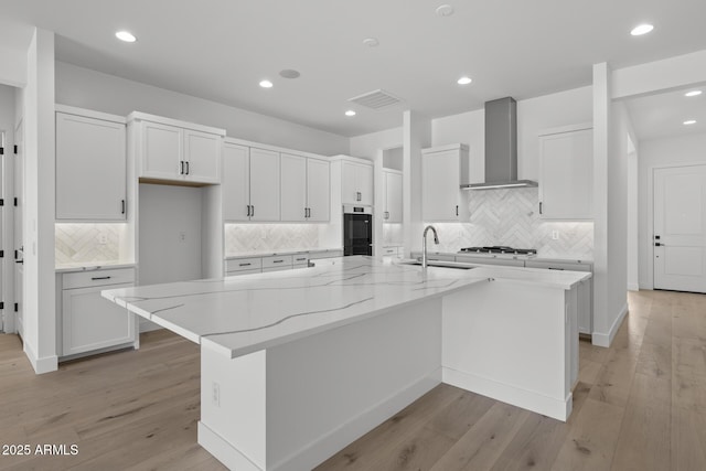 kitchen with light stone counters, light wood-style floors, white cabinets, a large island, and wall chimney exhaust hood