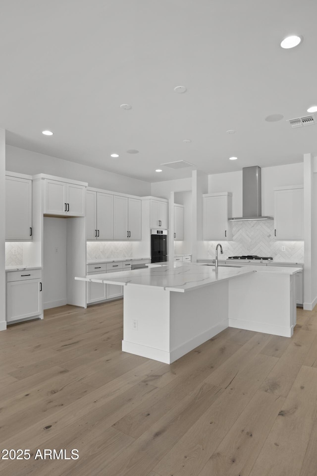 kitchen featuring a spacious island, wall chimney exhaust hood, and white cabinetry