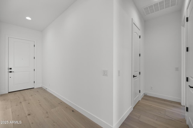 corridor with light wood-type flooring, visible vents, and baseboards