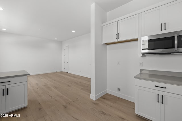 kitchen featuring baseboards, stainless steel microwave, light wood-type flooring, and white cabinets