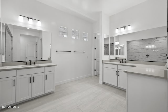 bathroom featuring a marble finish shower, two vanities, a sink, and baseboards