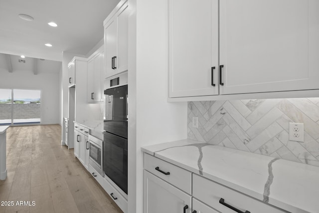 kitchen featuring light stone counters, stainless steel microwave, backsplash, light wood-style floors, and white cabinetry