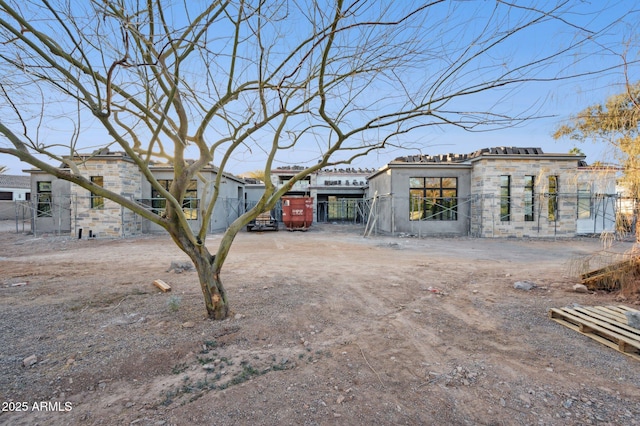 view of front facade featuring driveway, stone siding, fence, and stucco siding