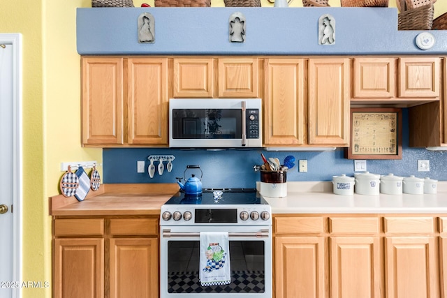 kitchen with stainless steel microwave, electric range oven, and light brown cabinets