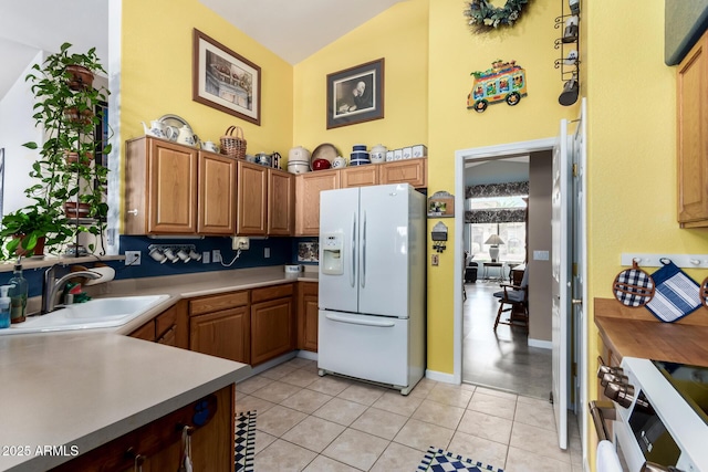 kitchen with a sink, light countertops, a towering ceiling, white fridge with ice dispenser, and range